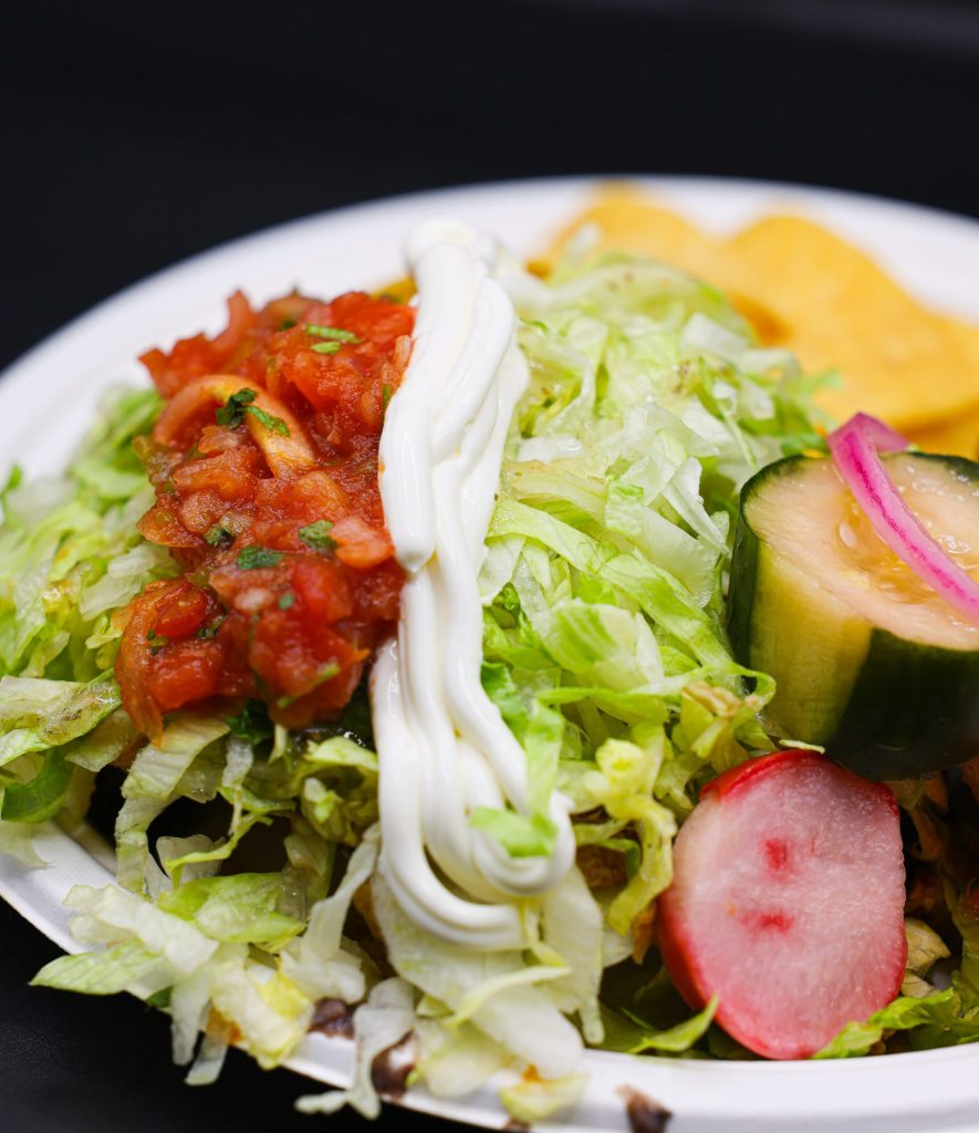 Tostada topped with sour cream, pico de gallo, lettuce and cucumber salad